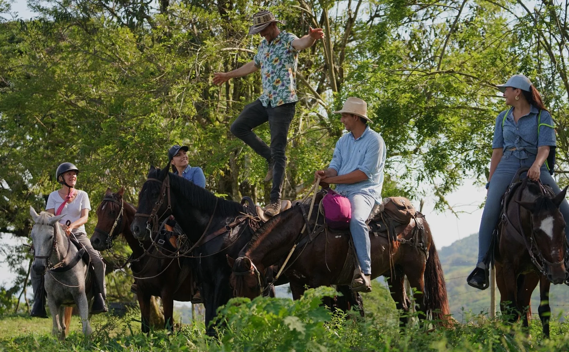 Riders resting their horses in a green clearing, one rider standing up on his saddle.