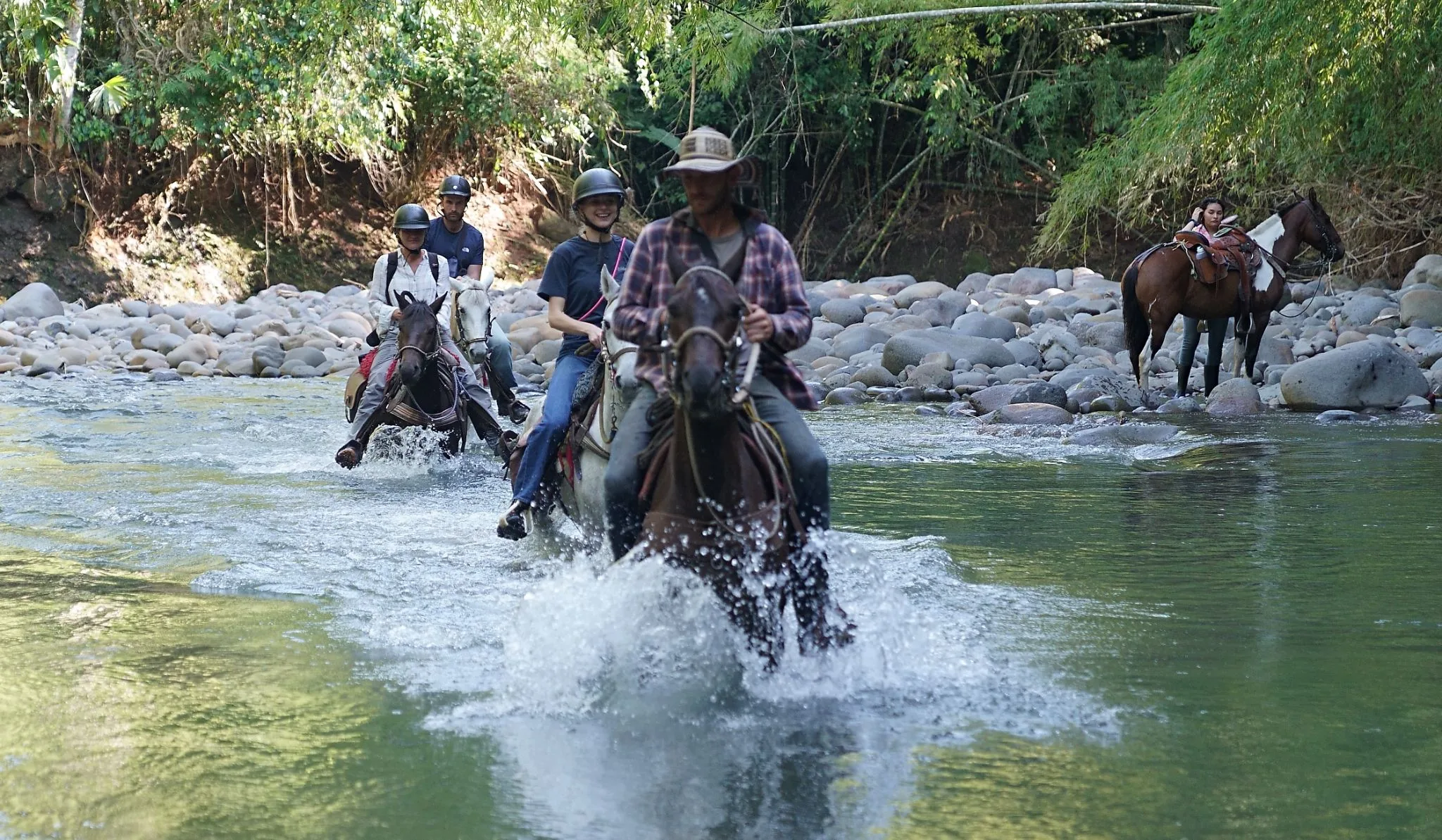 Three riders splashing across a shallow rocky river.